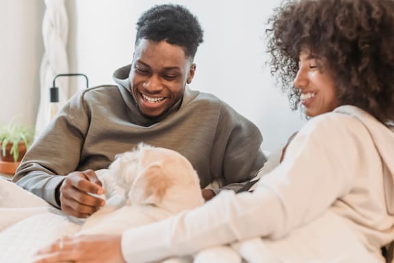 A man and woman are sitting on a bed with a dog between them.