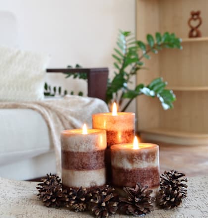 Three candles are lit and placed in a holder with a decorative wreath.