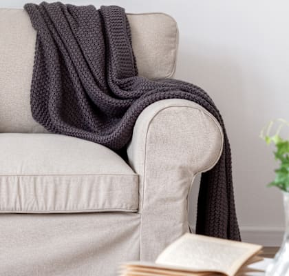 A grey couch with a grey blanket and a pillow is in the image.