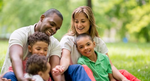 A family of four is sitting on the grass in a park.