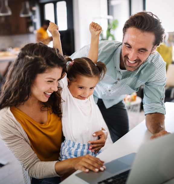 A family of three is gathered around a laptop in a modern kitchen.