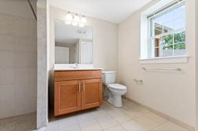 A large bathroom with full-size vanity, a window, overhead mirror lighting, tile flooring, and a stand-up shower.