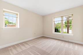 A bedroom with neutral carpet flooring and two windows providing ample natural light.