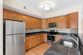 A U-shaped kitchen with stainless steel appliances, granite countertops, modern wooden cabinets, and hardwood-style flooring.