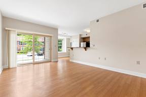 A spacious living room with hardwood style flooring and large sliding glass doors to a private patio near a dining area and kitchen.