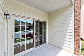 The exterior view of a patio with an outdoor light and large sliding glass doors to a living room.