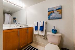 A bathroom with a full-sized mirror, spacious vanity with under-cabinet storage space, a towel bar, tile flooring, and a toilet.