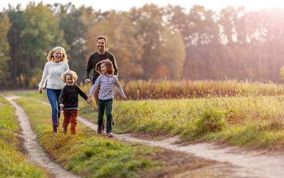 A family of four is walking down a dirt road holding hands.