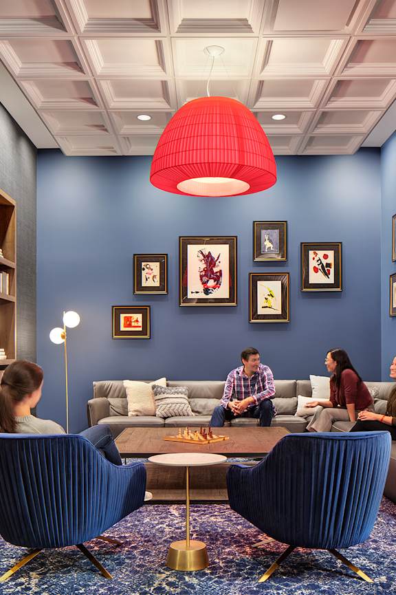 A group of people are sitting in a blue room with a red lamp hanging from the ceiling.