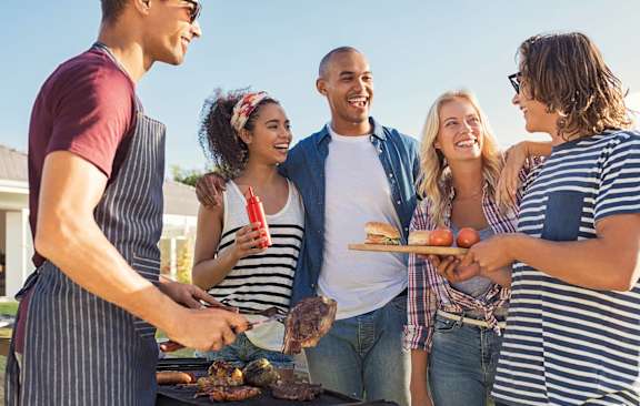 A group of people are gathered around a grill, enjoying a meal together.