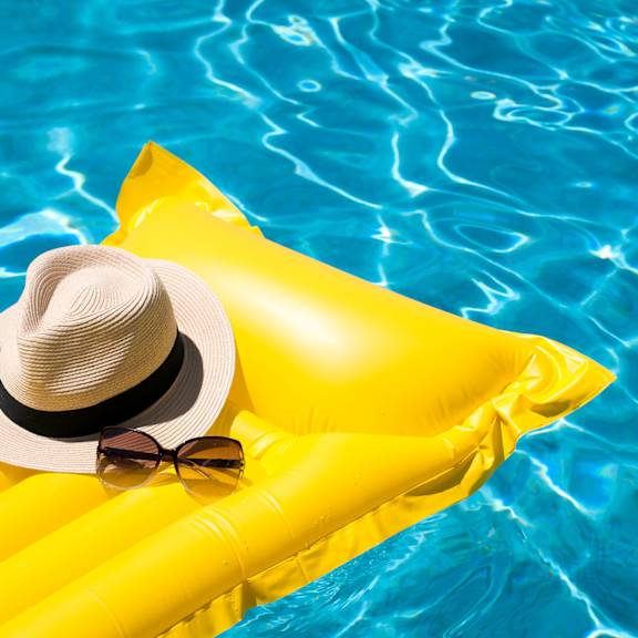 A woman in a straw hat and pink bikini holding a drink by a pool.