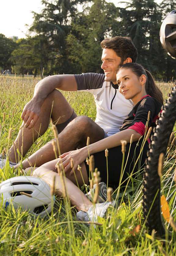 A man and a woman are sitting in the grass with their bikes.