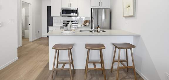 A kitchen with white cabinets and a white island with two stools.