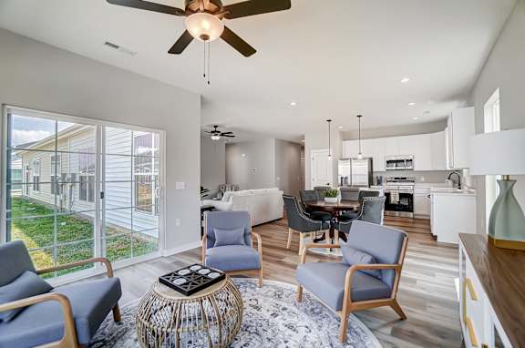 A modern living room with a ceiling fan and a dining area in the background.