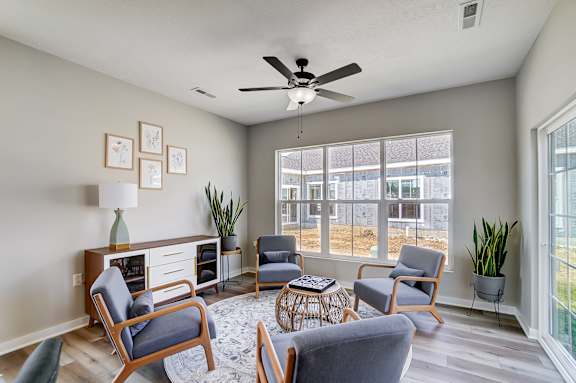A living room with a ceiling fan and a view of a building outside the window.