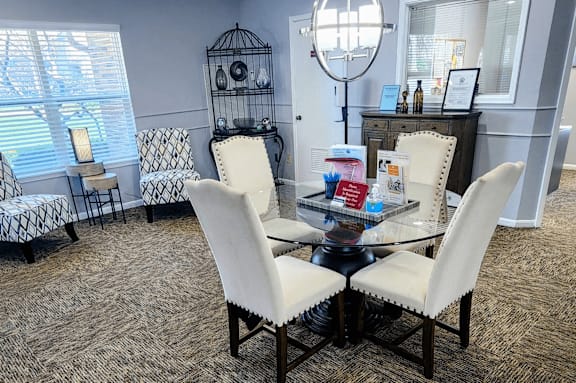 Clubhouse lounge at Skyler Ridge featuring a glass coffee table and white accent chairs with natural lighting.