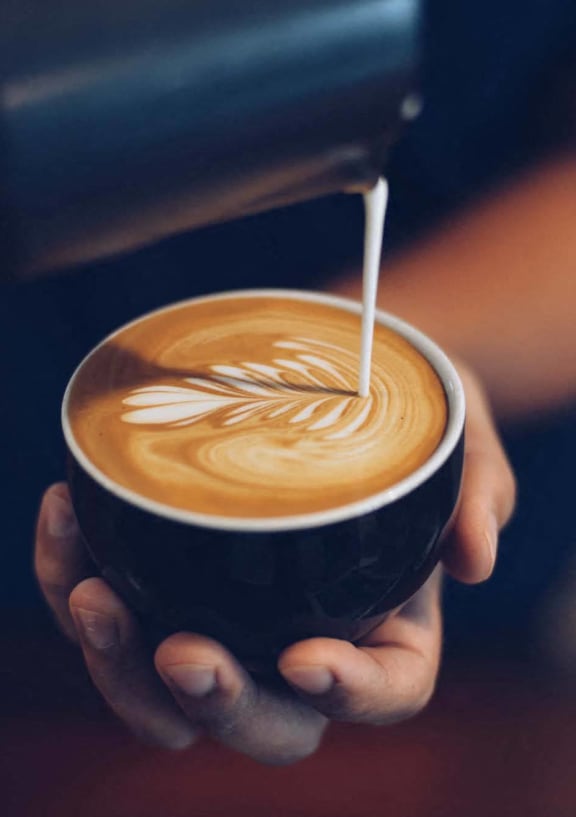 a person holding a cup of coffee with milk being poured into it