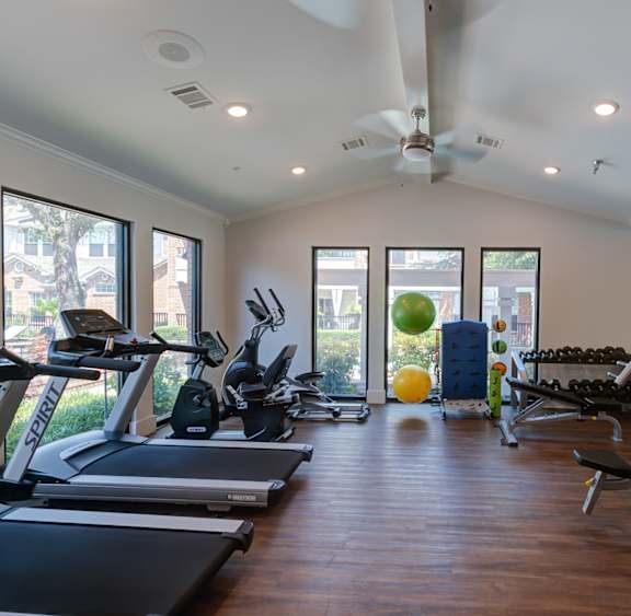 a gym with cardio equipment and a ceiling fan