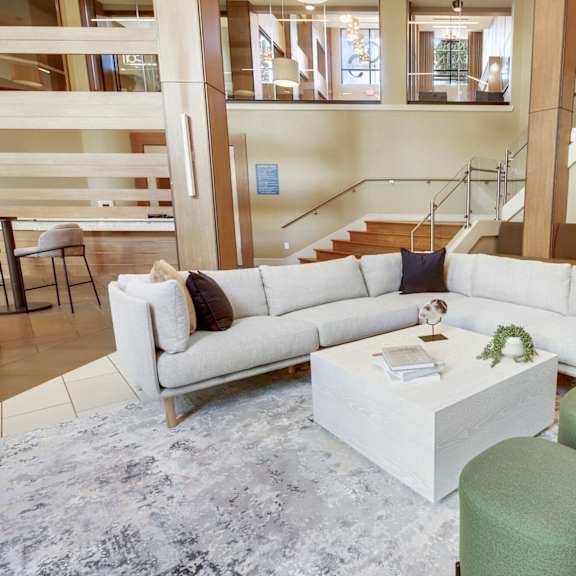A white sofa with a green ottoman and a white coffee table in a spacious room.