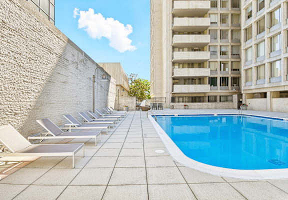 A pool surrounded by sun loungers and a brick wall.