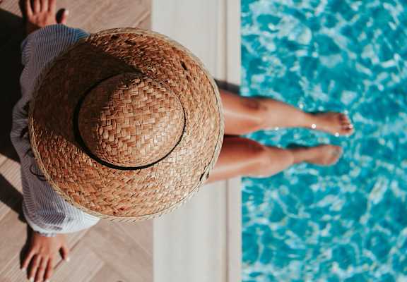 Woman in Sun Hat Sitting By Side Of Pool