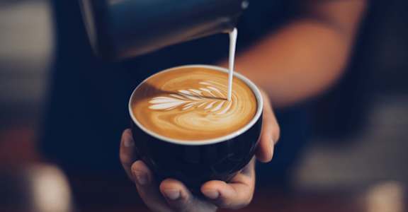 a barista pours milk into a coffee cup