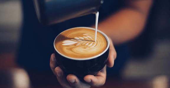 a person holding a cup of coffee with milk being poured into it