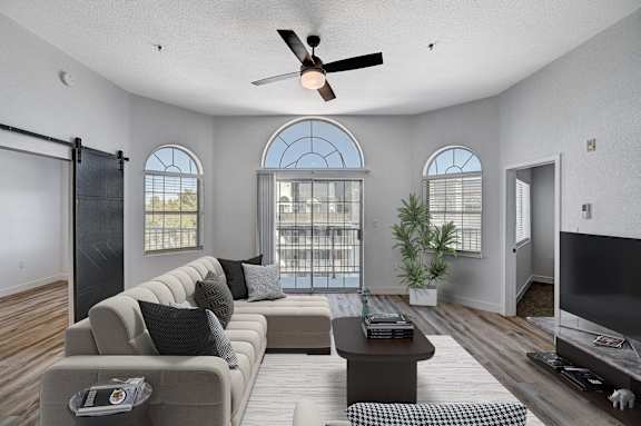 A living room with a grey sofa, a coffee table, a ceiling fan, and a sliding glass door.