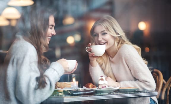 Two Women Laughing Together While Sitting in Coffee Shop