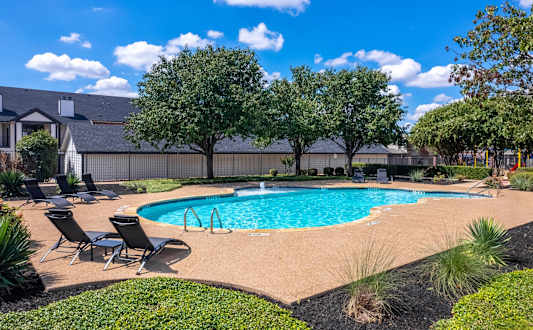 A swimming pool surrounded by trees and lawn chairs.
