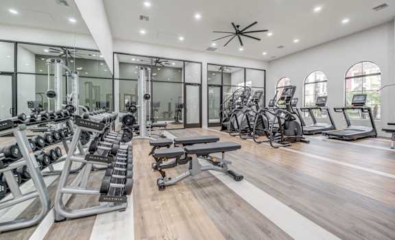 A gym with cardio machines, TVs, and weights at Desert Club.