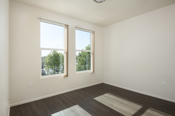 an empty room with two windows and wood floors