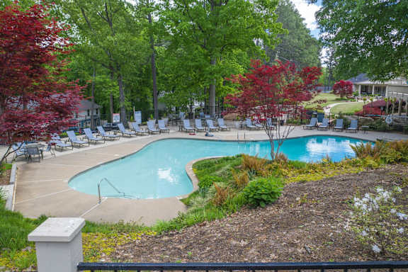 A pool surrounded by trees and lawn chairs.