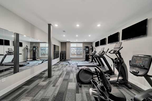 A spacious gym with treadmills, elliptical machines, and mirrors.