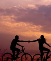 a man and woman holding hands while riding bikes at sunset