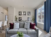 Thumbnail 12 of 21 - Grey couch with red and blue pillows is in the center of a well-lit room with a dining table and chairs at 200 City View, Provo, UT