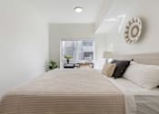 Thumbnail 12 of 25 - A bed with a beige comforter and two pillows in a room with a window.
