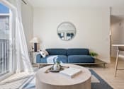 Thumbnail 7 of 25 - A living room with a blue couch and a round table with a book on it.