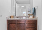 Thumbnail 21 of 26 - A bathroom with a brown vanity and a mirror above it.