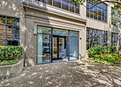 Thumbnail 15 of 25 - A building entrance with glass doors and a concrete walkway.