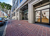 Thumbnail 3 of 25 - A red brick walkway leads to a building with a glass door entrance.