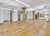 Thumbnail 8 of 25 - A room with wooden floors and white walls with columns in the middle.