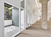 Thumbnail 24 of 25 - A long hallway with a stone pillar and glass doors.