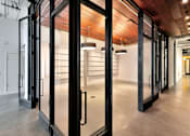 Thumbnail 19 of 25 - A long hallway with black doors and a wooden ceiling.