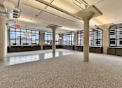 Thumbnail 22 of 25 - A large, empty room with concrete pillars and a carpeted floor.