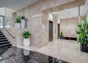 Thumbnail 13 of 15 - A hallway with marble floors and walls, a staircase, and potted plants.