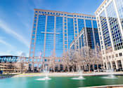 Thumbnail 2 of 24 - A large glass building with a fountain in front of it.