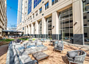 Thumbnail 4 of 24 - A large outdoor seating area with couches and tables is surrounded by tall buildings.