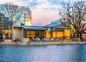 Thumbnail 7 of 24 - A modern building with a glass facade is reflected in the water in front of it.