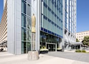 Thumbnail 7 of 18 - A large building with a glass facade and a tall sculpture in front.